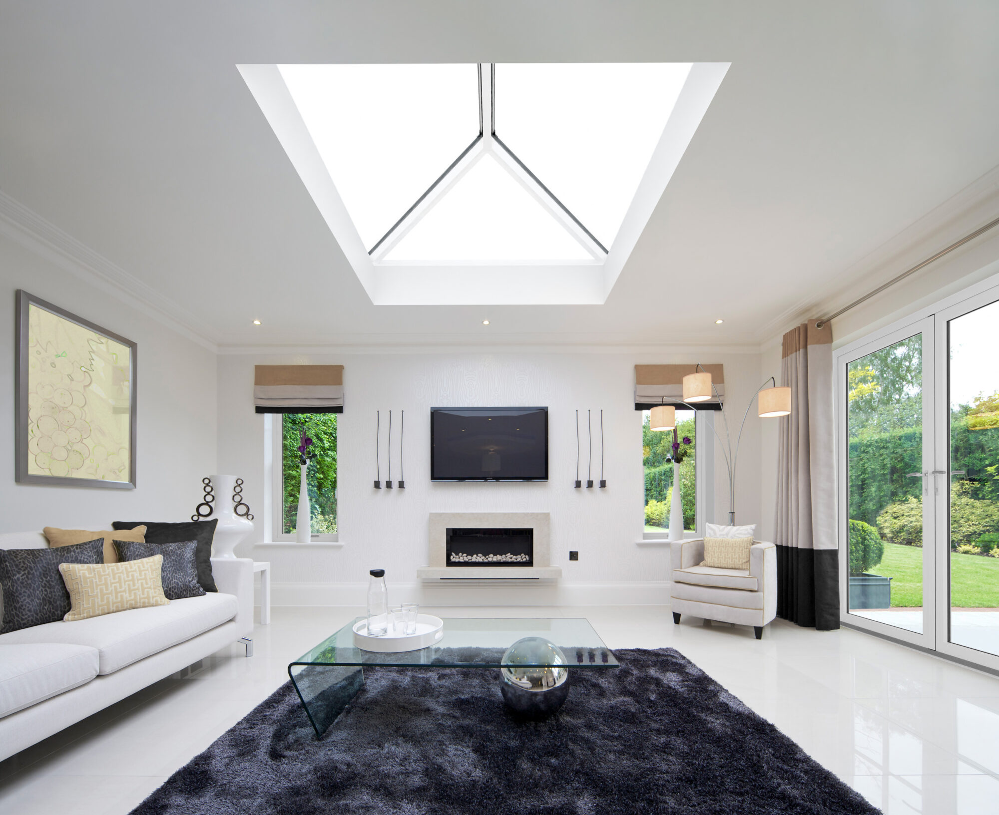 "a beautifully laid out modern family room in an exclusive new home. a large skylight overhead allows plenty of light whilst a large dark grey rug below creates a comfortable feel. The colour theme of the room is white with yellows, dark purple and greys. The walls are white and the floor is cream coloured marble. The lights of the standing lamp have been switched on for effect. There is a property release for the artwork on the wall.Looking for a Living Room image Then please see my other Living Room and related images by clicking on the Lightbox link below..."